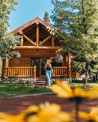 Rustic log cabin at Baker Creek By Basecamp with stone foundation, red roof, and pine forest backdrop.