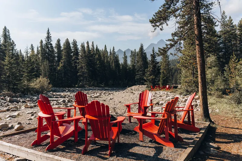 Baker Creek By Basecamp red Adirondack chairs on gravel overlook with forested mountains in background.