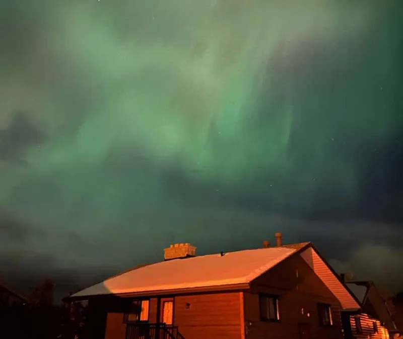 Northern lights shimmer green above a log chalet at Becker's Chalets in Jasper.