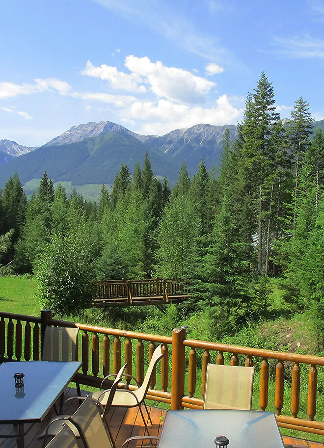 Wooden deck with table and chairs overlooking forested valley and snow-capped Rocky Mountain peaks at Cross River Wilderness Centre.