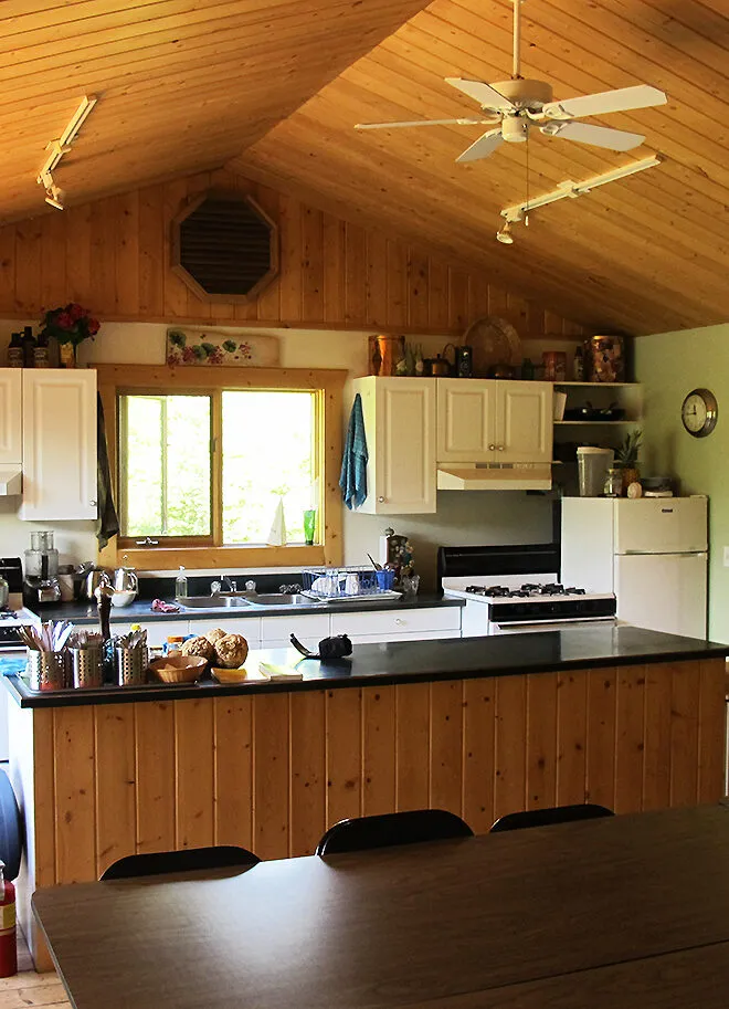 Wooden kitchen interior at Cross River Wilderness Centre with log walls, black counters, and vaulted timber ceiling.