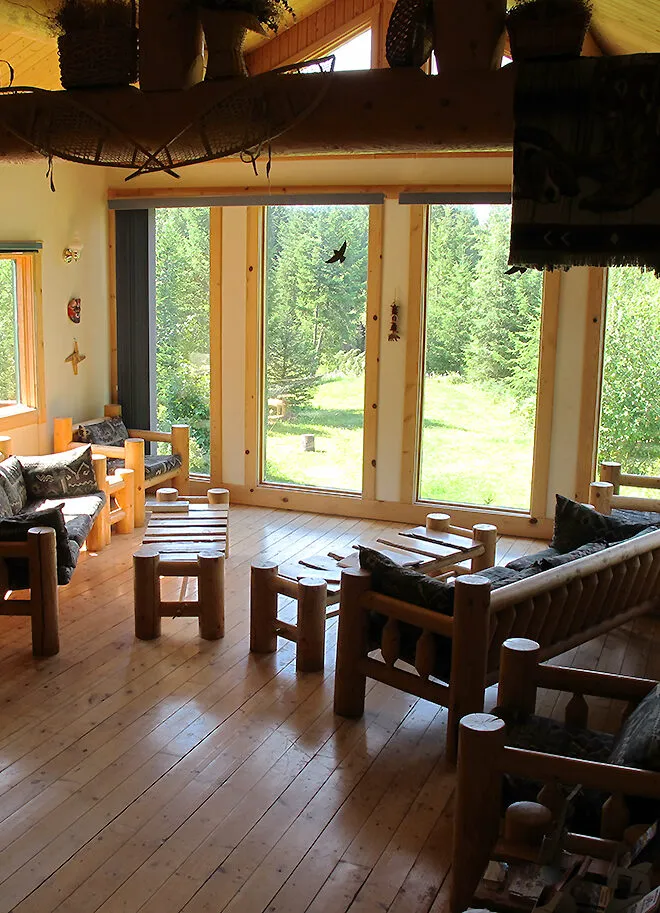 Cross River Wilderness Centre living room with timber frame, wood furniture, and expansive forest views through glass doors.