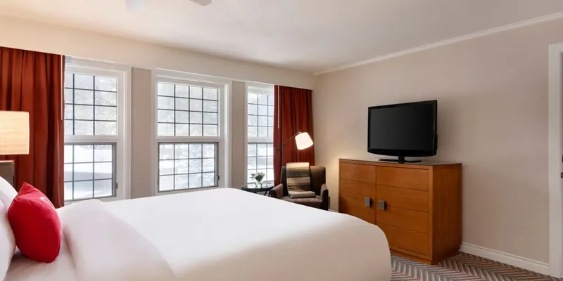 Fairmont Jasper cabin bedroom with white bed, large windows overlooking lake, wooden dresser and television.