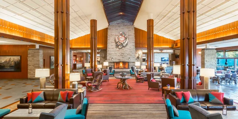 Fairmont Jasper Park Lodge lobby with massive timber columns, central stone fireplace, and red carpeted seating areas.