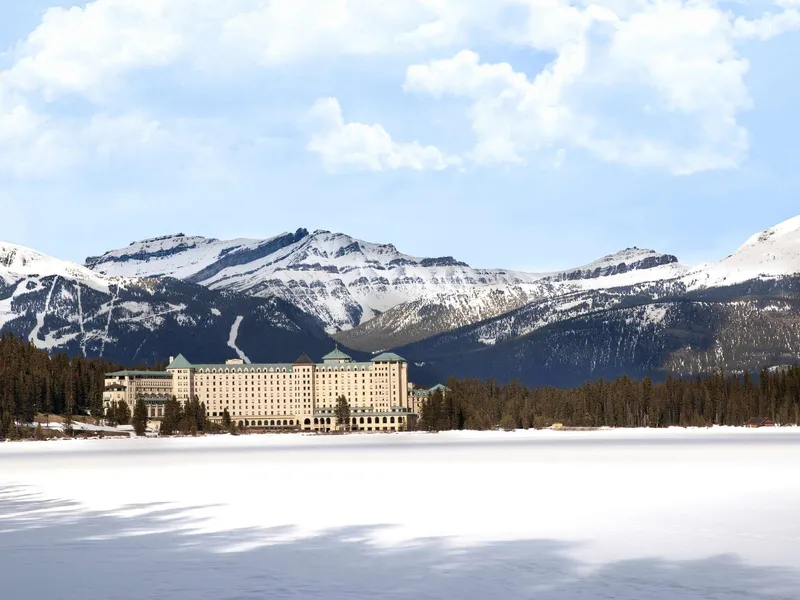 Fairmont Chateau Lake Louise stone château on frozen lake with snow-capped peaks beyond.
