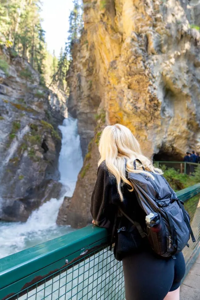 Visitor overlooking Johnston Canyon Lodge's namesake waterfall from a railing amid layered canyon walls.