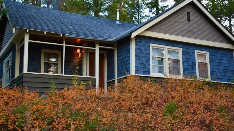 Johnston Canyon Lodge bungalow with blue shingle siding, covered porch, and autumn foliage.