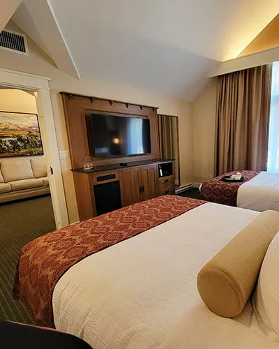 Kilmorey Lodge double-queen suite with two beds, wood entertainment unit, and tan curtains.