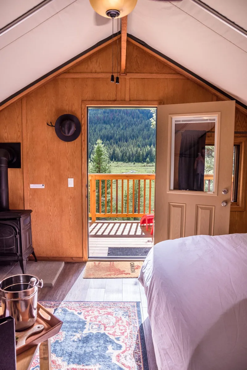 Interior of Mount Engadine Lodge's timber glamping tent with conifer forest view through glass doors.