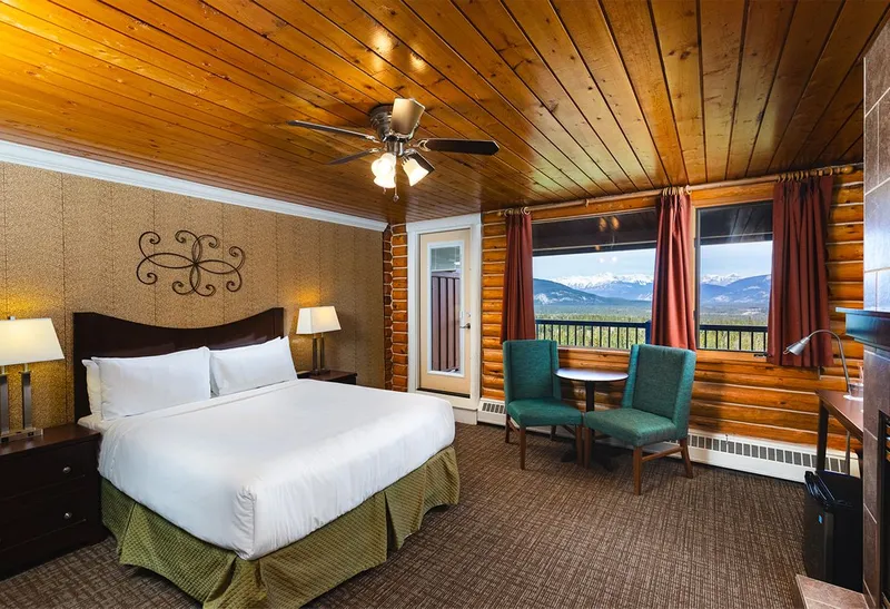 Log cabin bedroom at Overlander Lodge with mountain views framed by windows and forest beyond.