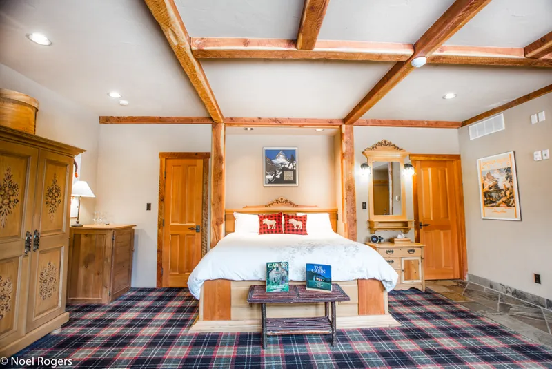 Paintbox Lodge bedroom with timber beam ceiling, wood furniture, tartan rug, and mountain artwork.