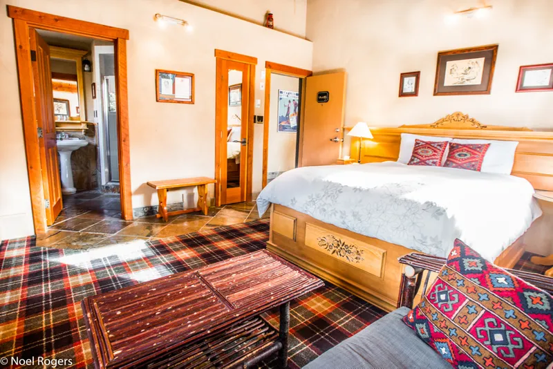 Paintbox Lodge bedroom with wood bed frame, tartan carpet, orange wood accents, and Native patterned textiles.