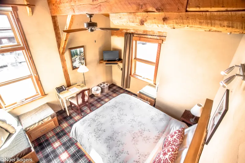 Paintbox Lodge guest room with exposed timber beams, plaid floor, bed with wood nightstands, and windows.