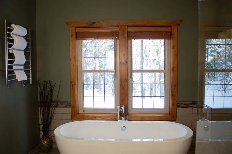 Freestanding oval soaking tub at Prairie Creek Inn's Birchside Cottage with wood-framed windows overlooking winter forest.
