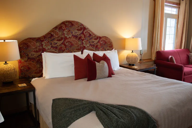Cozy bedroom at Prairie Creek Inn with upholstered headboard, burgundy pillows, and warm lighting.