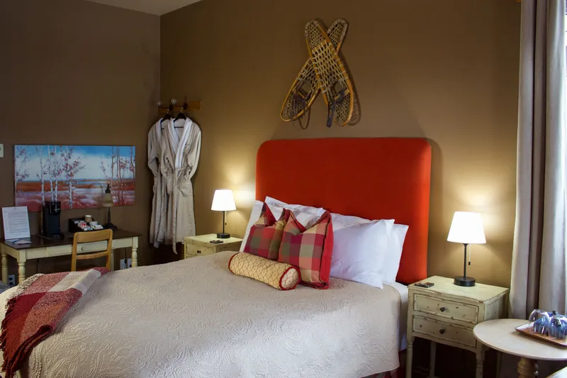 Prairie Creek Inn Canadiana Suite bedroom with red upholstered headboard and snowshoe wall decor.