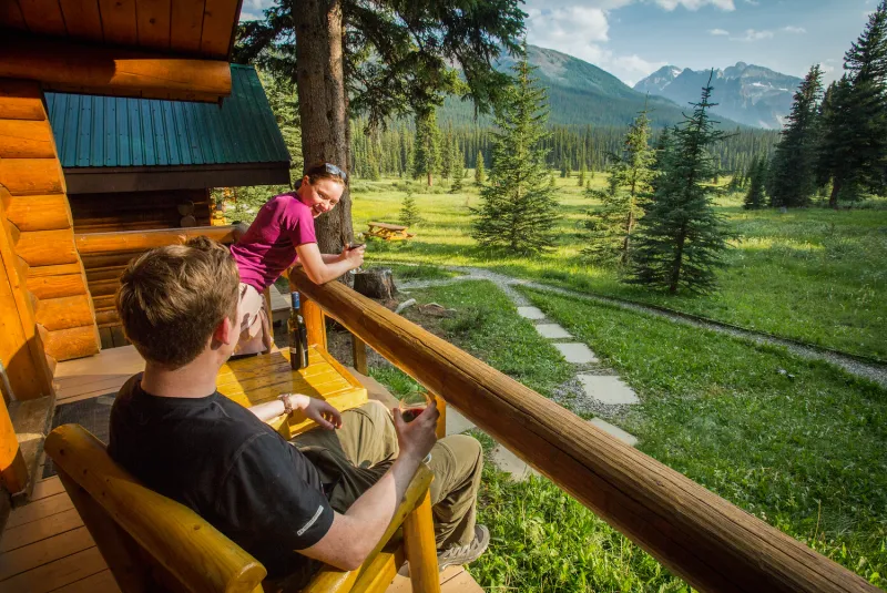 Shadow Lake Lodge log cabin deck overlooks alpine meadow, coniferous forest, and mountain peaks.