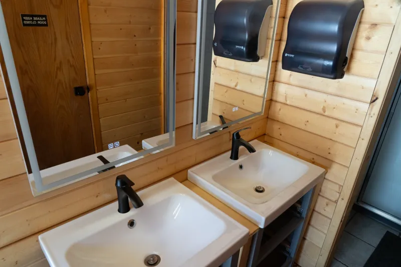 Shadow Lake Lodge log cabin bathroom with dual sinks, black faucets, and wooden walls.