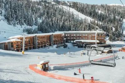 Sunshine Mountain Lodge's modern timber lodge with snowy ski runs, chairlifts, and snow-covered mountain forest.